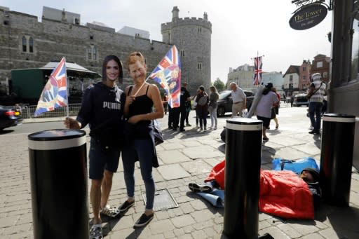 A couple wearing masks of Britain's Prince Harry and US actress Meghan Markle pose with Union flags near Windsor Castle on May 18, 2018, the day before the Royal wedding
