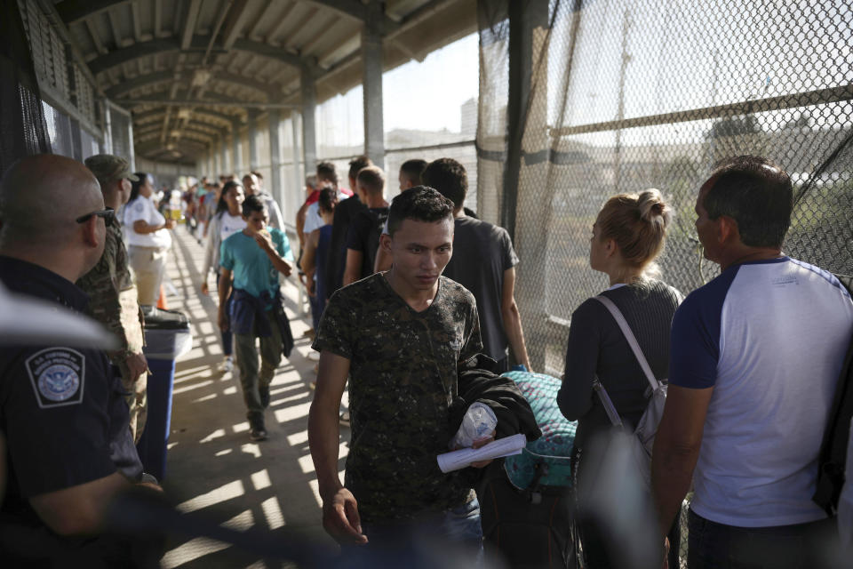 FILE - In this Aug. 2, 2019 file photo, migrants return to Mexico as other migrants line up on their way to request asylum in the U.S., at the foot of the Puerta Mexico bridge in Matamoros, Mexico, that crosses into Brownsville, Texas. Some asylum seekers were told by officials Friday, March 5, 2021, that the U.S. government may reopen their cases and they would eventually be able to enter the U.S. to wait out the asylum process. (AP Photo/Emilio Espejel, File)