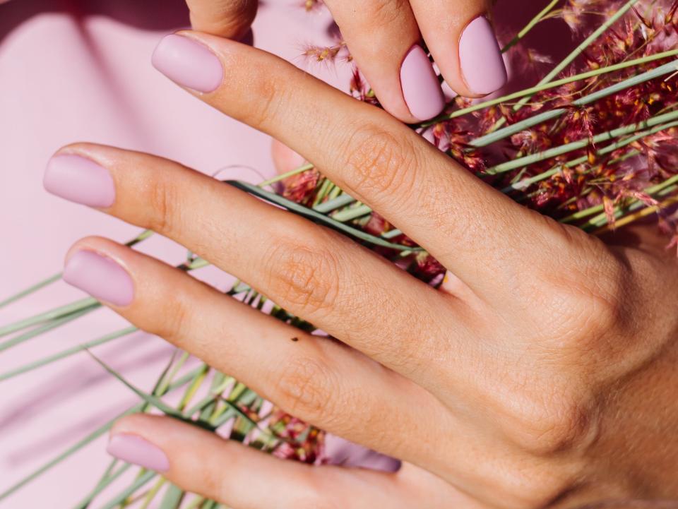 Woman holding flowers with pastel purple nails.