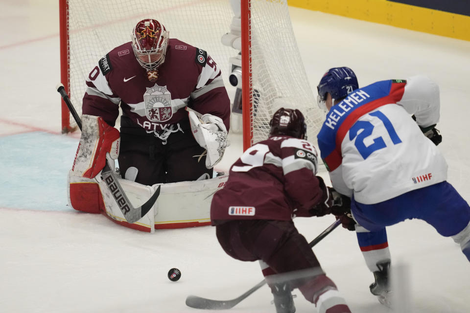 Latvia's goalkeeper Kristers Gudlevskis, left, makes a save in front of Slovakia's Milos Kelemen, right, during the preliminary round match between Slovakia and Latvia at the Ice Hockey World Championships in Ostrava, Czech Republic, Sunday, May 19, 2024. (AP Photo/Darko Vojinovic)