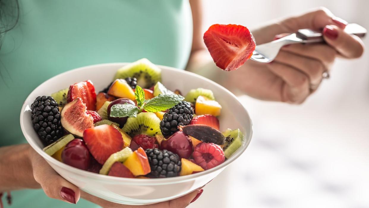 a woman breakfasts a fruit salad high in vitamins and fiber