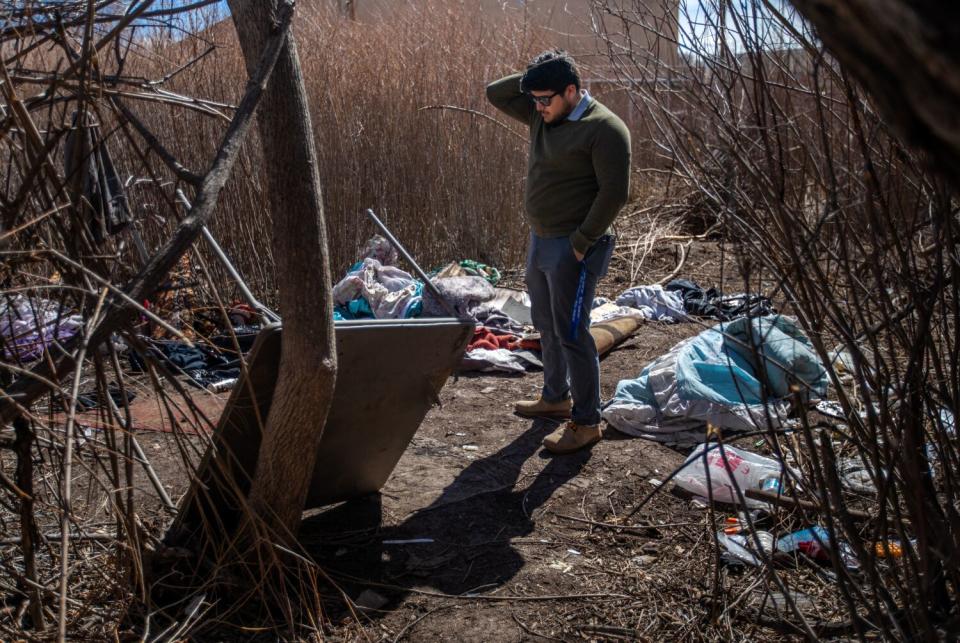 A man stands amid debris at a homeless camp