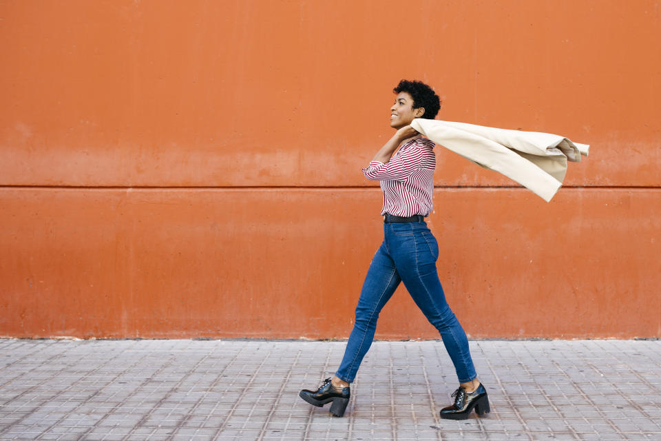 Businesswoman walking at a red wall in the background, putting her jacket on her shoulder