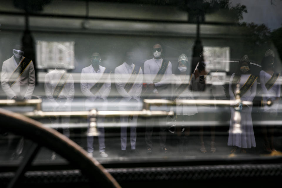 Wearing sashes and tiaras, the Kings and Queens of Models Inc., are reflected in a horse drawn hearse from Compassion and Serenity Funeral Home as they pay their respects to Joanne Paylor, 62, of southwest Washington, during her funeral in Suitland-Silver Hill, Md., Sunday, May 3, 2020. Models Inc. is a community organization founded by Iran "Bang" Paylor that was supported by his mother, Joanne Paylor. Despite not having died from coronavirus, almost every aspect of her funeral has been impacted by the pandemic. (AP Photo/Jacquelyn Martin)