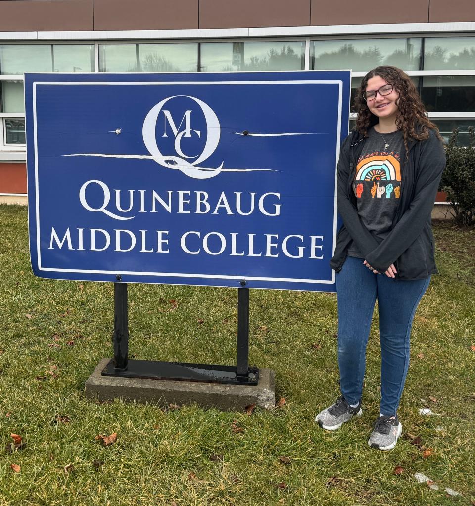 Lexi Barber, a freshman at Quinebaug Middle College magnet high school in Danielson, stands next to the school's sign.