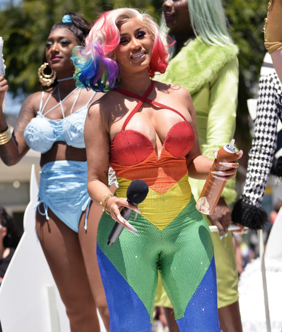 Cardi B in a rainbow bodysuit and rainbow wig holding a microphone