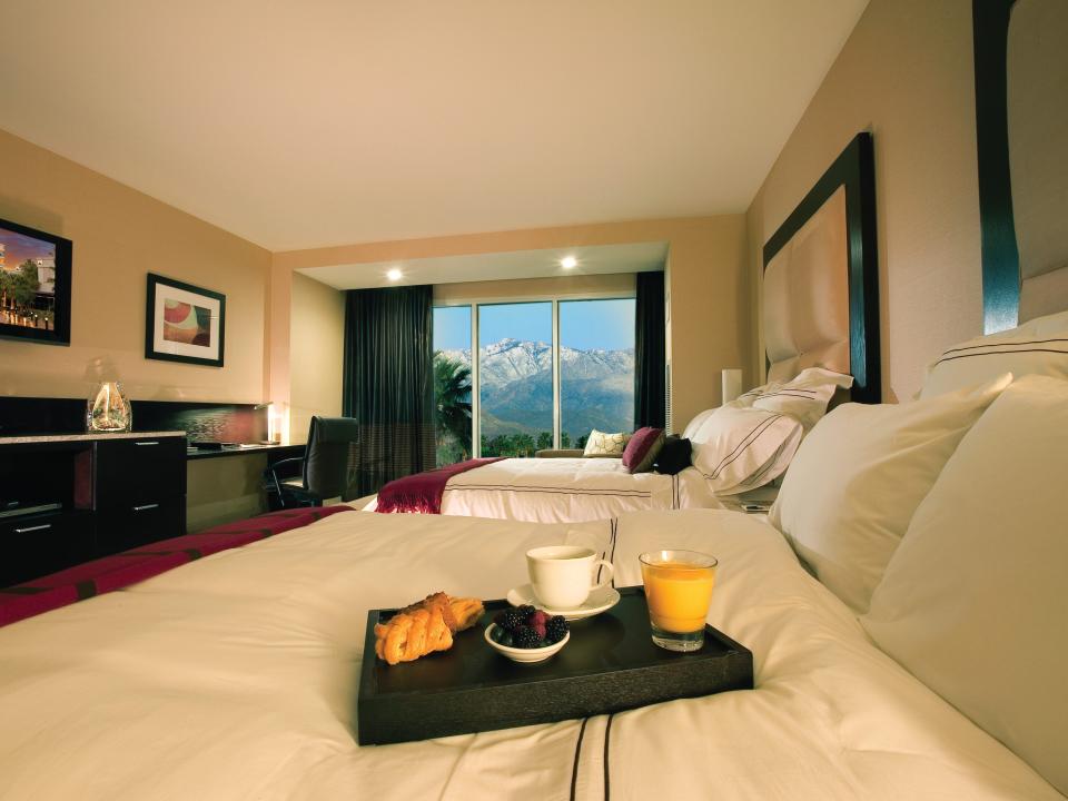 Two beds with a tray of food and a balcony with windows featuring mountain views.