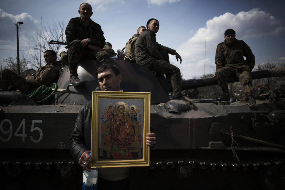 Un residente de Kramatorsk, Ucrania, sostiene una imagen de la religión ortodoxa frente a un vehículo blindado tripulado por soldados del ejército ucraniano el miércoles 16 de abril de 2014. (Foto de AP/Manu Brabo)