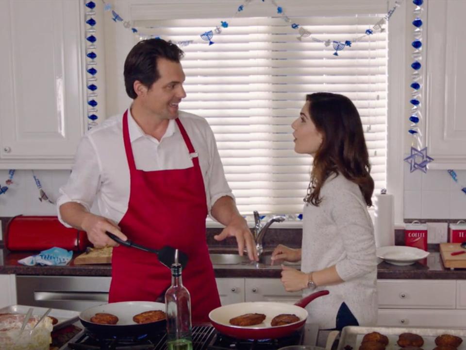 A scene from Hallmark's "Double Holiday." A man flips latkes with Hanukkah decorations in the background.