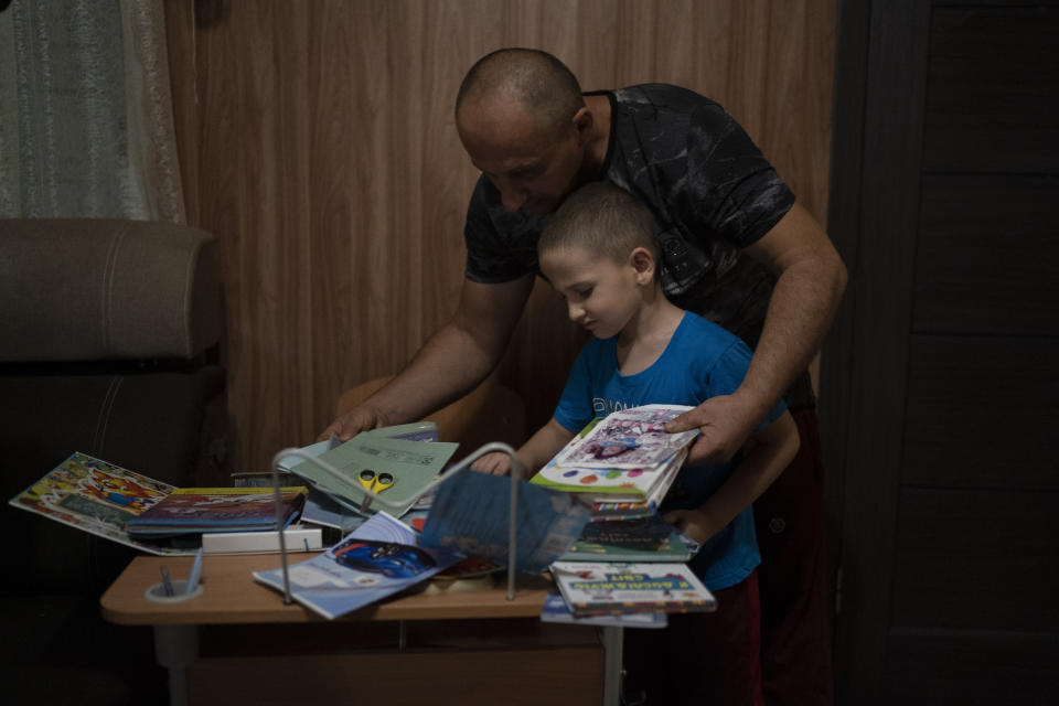Oleksii Makarov, 6, displays his books and scholar materials on his student desk, that he uses for online classes, as he stands with his father Rodion Makarov, 45, at their home in Kramatorsk, Ukraine, Sunday, Aug. 28, 2022. The School Number 23, the same that where his parents also studied, was destroyed after a Russian attack that occurred in the second half of July. (AP Photo/Leo Correa)