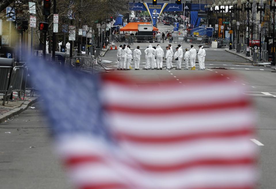Law enforcement evidence technicians are seen behind a U.S. flag placed at a memorial for the victims as they continue search the scene of the Boston Marathon bombings for evidence in Boston, Massachusetts, in this April 20, 2013 file photo. The trial of accused bomber Dzhokhar Tsarnaev, a 21-year-old ethnic Chechen who is a naturalized U.S. citizen, begins this month. Tsarnaev could get the death penalty if convicted of killing three people and injuring more than 260 others by detonating a pair of homemade bombs placed amid a crowd of thousands of spectators at the race's finish line on April 15, 2013. He has pleaded not guilty to all 30 charges against him. REUTERS/Jim Bourg/Files (UNITED STATES - Tags: CRIME LAW CIVIL UNREST)