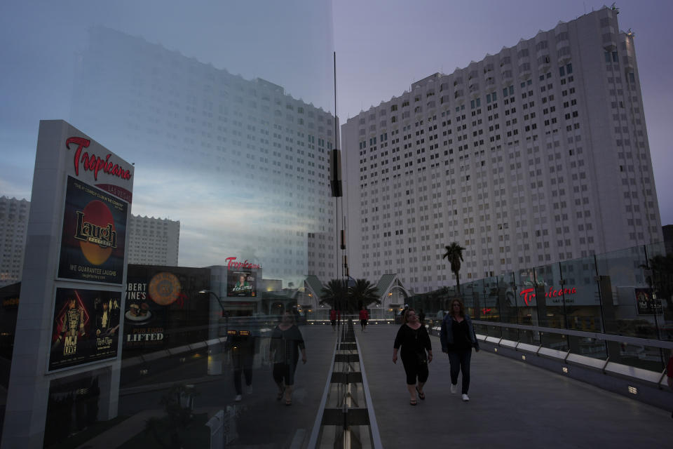 The Tropicana hotel-casino is reflected in glass as people walk on a pedestrian bridge along the Las Vegas Strip, Thursday, March 28, 2024, in Las Vegas. (AP Photo/John Locher)