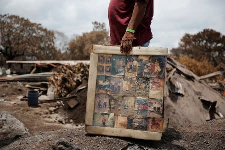 A resident holds framed pictures of his family, recovered from his house in an area affected by the eruption of the Fuego volcano, in San Miguel Los Lotes in Escuintla, Guatemala June 13, 2018. REUTERS/Luis Echeverria/Files