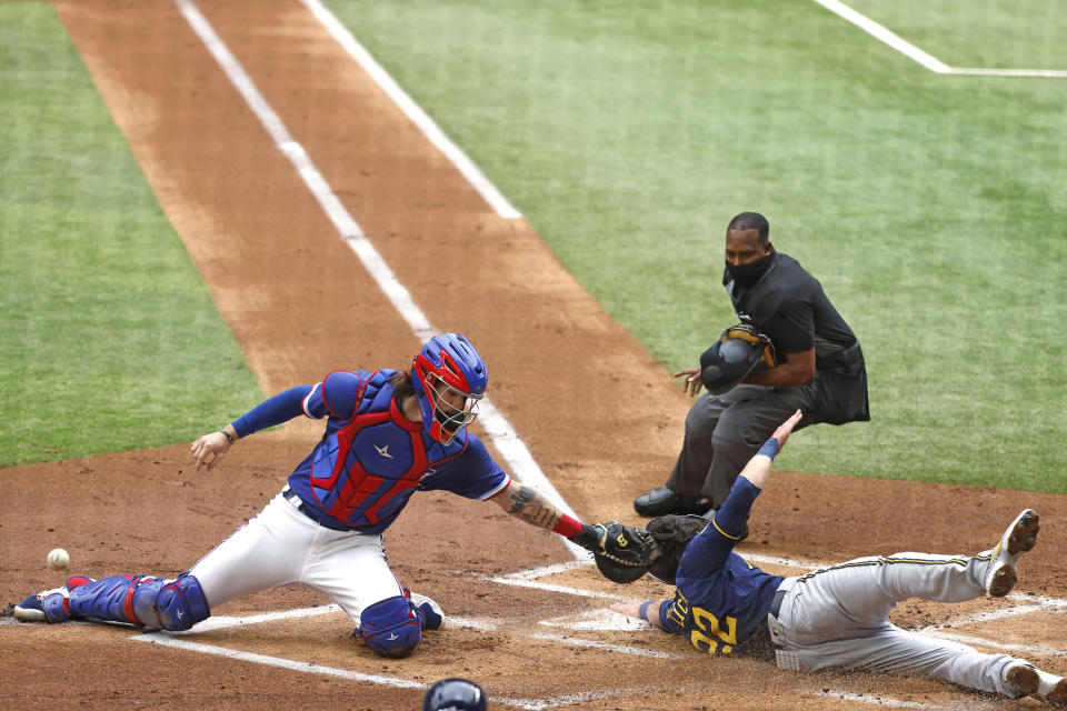 Milwaukee Brewers left fielder Christian Yelich (22) scores in front of Texas Rangers catcher Jonah Heim as home plate umpire Ramon De Jesus watches, during the first inning of a preseason baseball game Tuesday, March 30, 2021, in Arlington, Texas. (AP Photo/Michael Ainsworth)