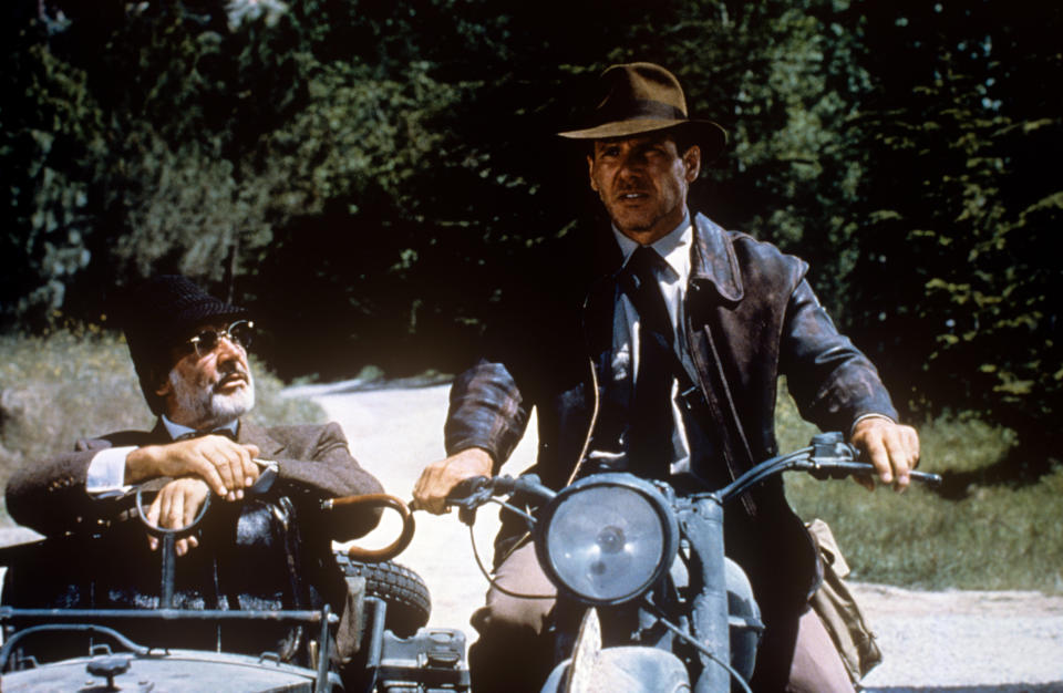 American actor Harrison Ford as archaeologist Indiana Jones riding the motorcycle in company of British actor Sean Connery as Prof. Henry Jones, Indiana's father, who gaves him a questioning look sitting on the sidecar, in a scene from the Indiana Jones and the Last Crusade. USA, 1989. (Photo by Mondadori Portfolio via Getty Images)