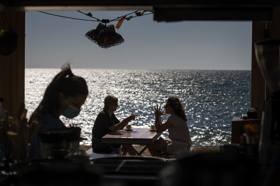 People sit on a terrace in a beach in Barcelona, Spain, on Wednesday, May 27, 2020. Roughly half of the population, including residents in the biggest cities of Madrid and Barcelona, are entering phase 1, which allows social gatherings in limited numbers, restaurant and bar service with outdoor sitting and some cultural and sports activities. (AP Photo/Emilio Morenatti)