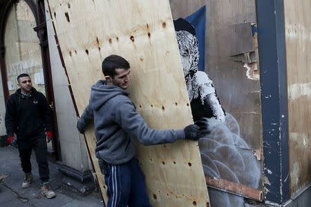 A worker carries a board to cover a new graffiti mural attributed to Banksy, opposite the French embassy in London, Britain January 25, 2016. REUTERS/Stefan Wermuth