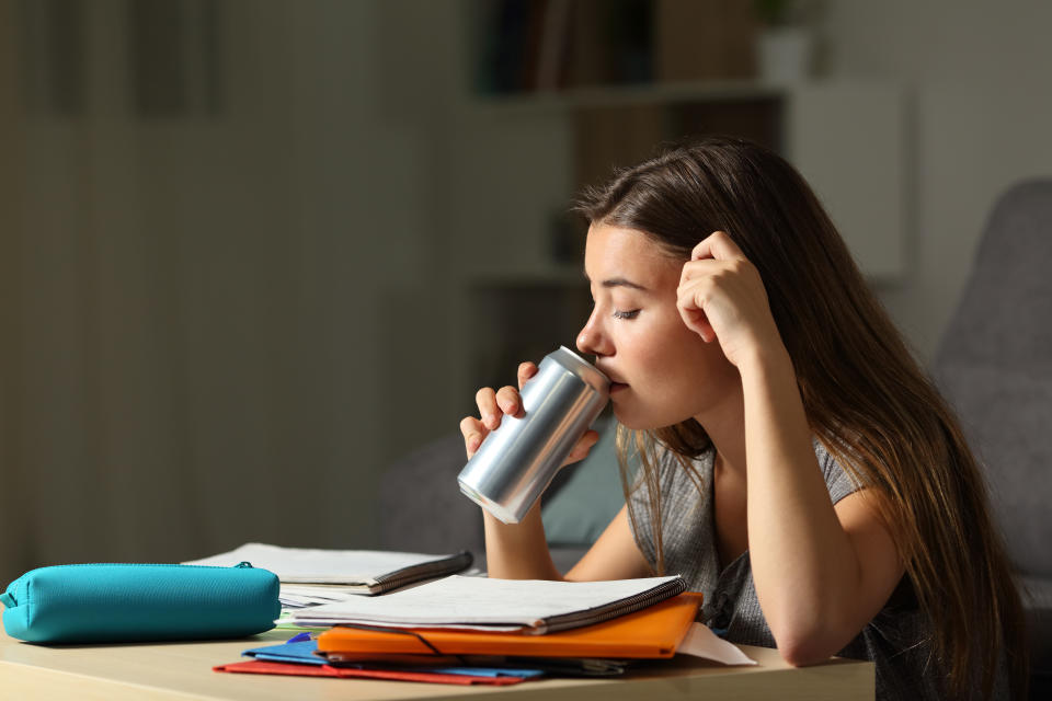 Studious teen studying drinking energy beverage while is studying in the night at home