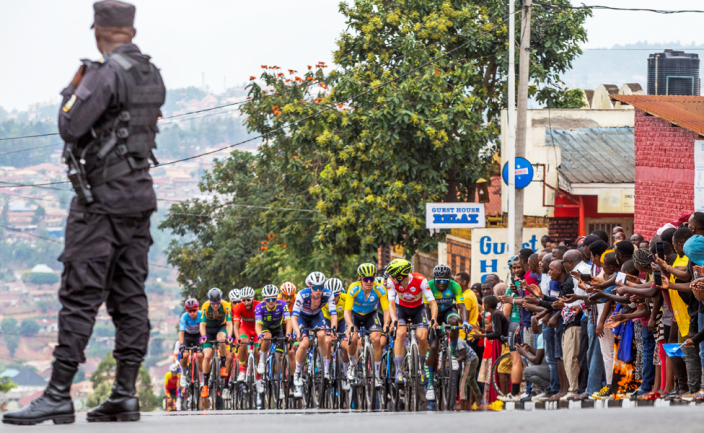 A security officer watches a cyclist competing in the Tour de Rwanda in Kigali, Rwanda - Saturday, February 25, 2023