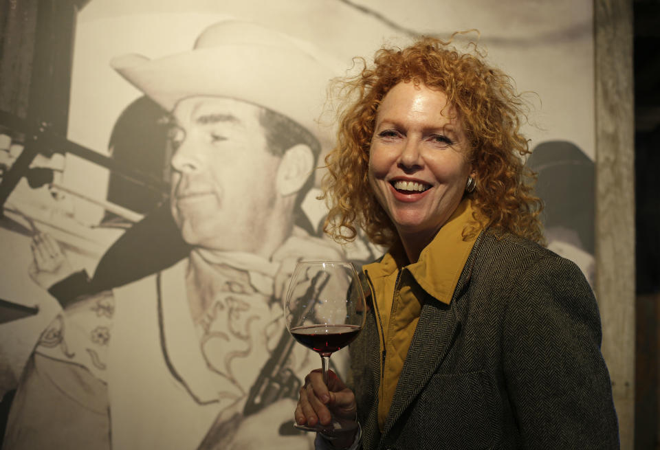 In this photo taken March 15, 2013 Kate MacMurray, daughter of the late actor Fred MacMurray poses with a glass of Pinot Noir by a photograph of her father in a tasting area and gallery of old photographs at the MacMurray Ranch in Healdsburg, Calif. The former cattle ranch, which was purchased in 1941 by the actor in the popular TV series "My Three Sons," now produces wine and is owned by the Gallo wine family. (AP Photo/Eric Risberg)