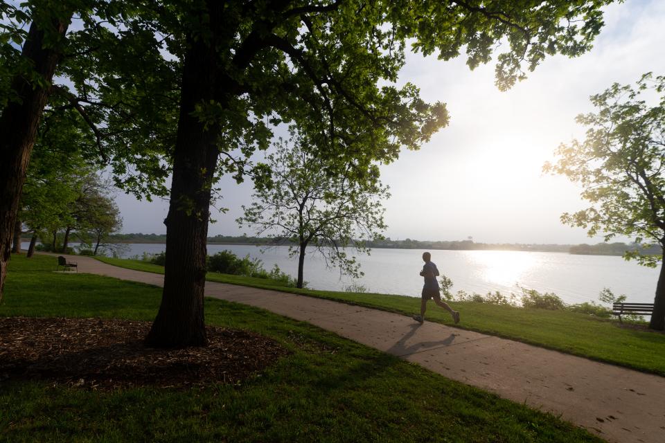 A runner follows the trail around Lake Shawnee Tuesday morning, avoiding the midday heat during a week when mercury readings here are expected to reach triple digits on Wednesday and Thursday.