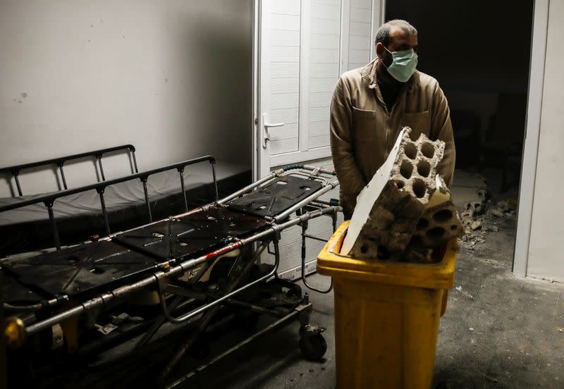 A construction worker cleans debris as he walks past a stretcher at the entrance of an operating room at a hospital in Idlib