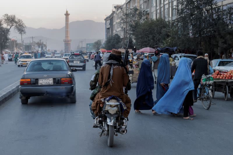 FILE PHOTO: A group of women wearing burqas crosses the street as members of the Taliban drive past