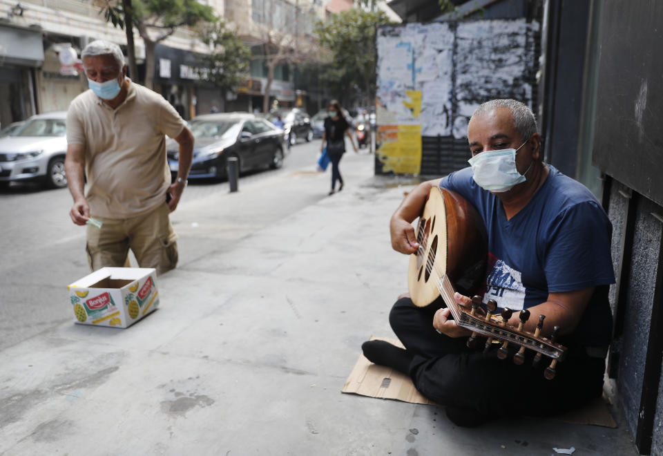 A street musician man performs with a mask on his face to help stop the spread of the coronavirus, as other man on the left puts money on a box, in Beirut, Lebanon, Wednesday, July 29, 2020. Lebanon is hurtling toward a tipping point at an alarming speed, driven by financial ruin, collapsing institutions, hyperinflation and rapidly rising poverty _ with a pandemic on top of that. The collapse threatens to break a nation seen as a model of diversity and resilience in the Arab world. (AP Photo/Hussein Malla)