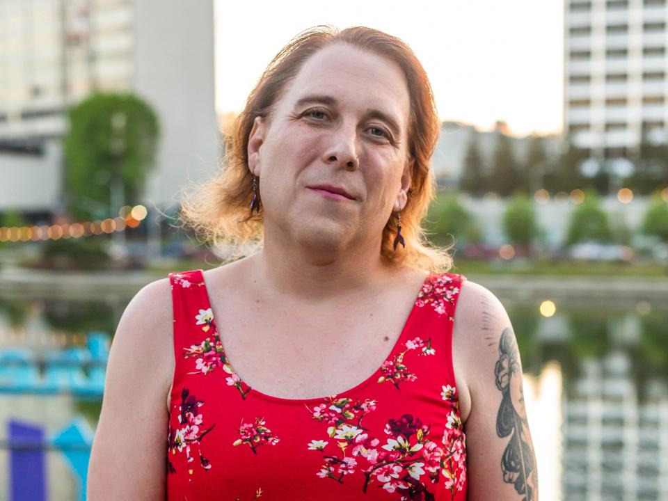 Amy Schneider poses against the backdrop of a cityscape while wearing a red floral dress.