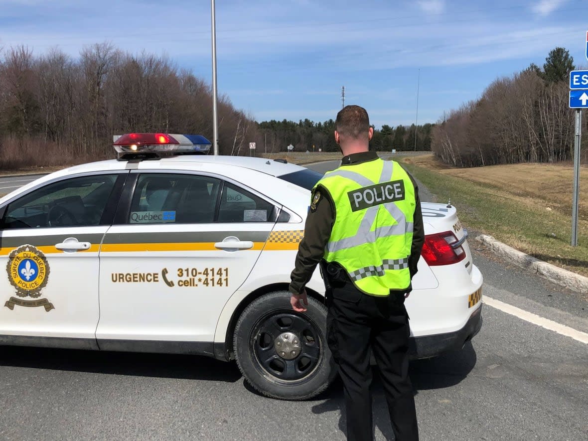 A police officer stands outside his vehicle where Highway 20 is blocked for an undertermined amount of time near Drummondville, about 100 kilometres northeast of Montreal. (Jean-François Dumas/Radio-Canada - image credit)