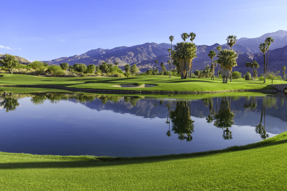 Golf course with water hazard, sand bunkers, and mountains in the background