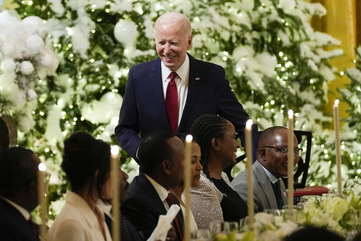 President Biden smiling while standing near a table where guests are seated.