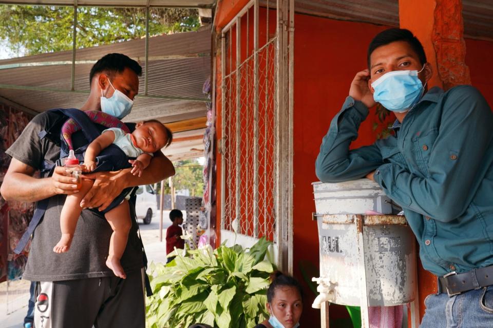 Honduran migrants, including one holding a baby, wait outside