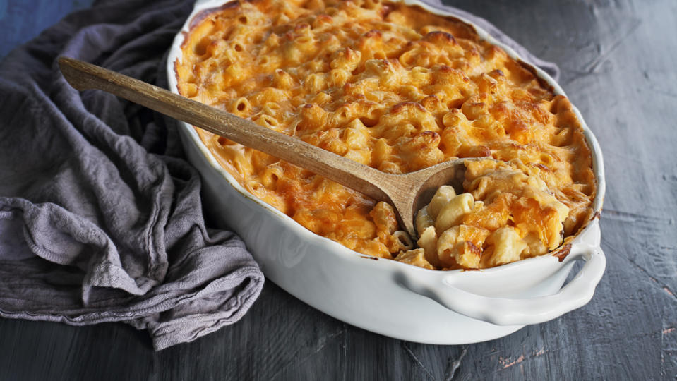 High angel view of a dish of fresh baked macaroni and cheese with table cloth and old wooden spoon over a rustic dark background. - Credit: Photo: courtesy Stephanie Frey/Adobe Stock