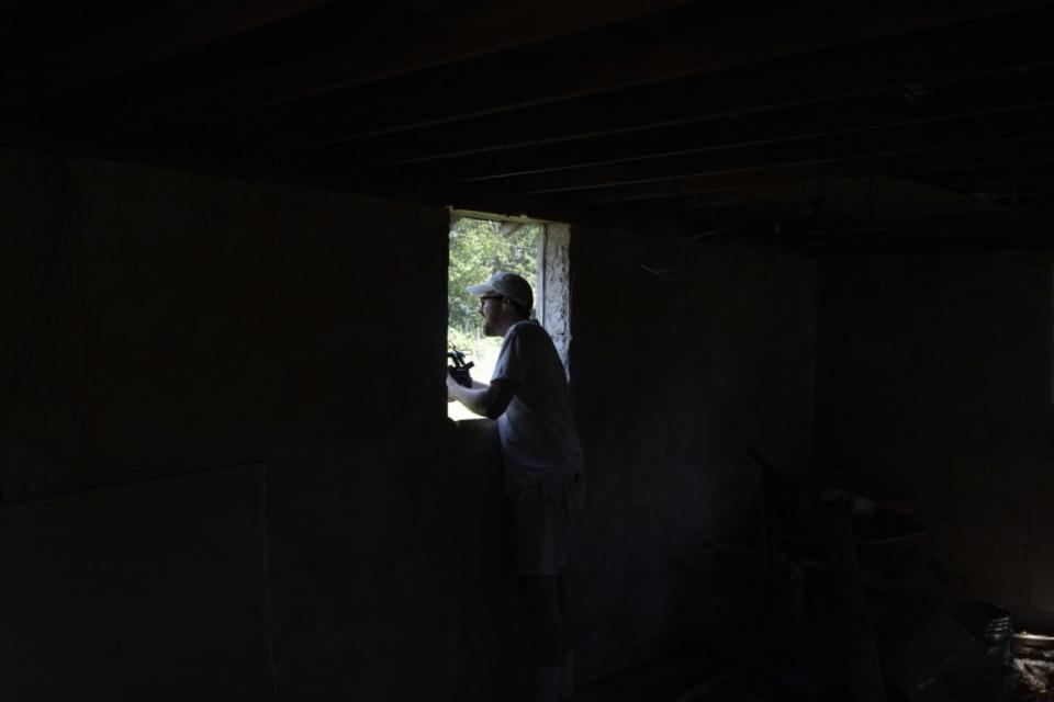 John Wilson stands in a dark house with a video camera.