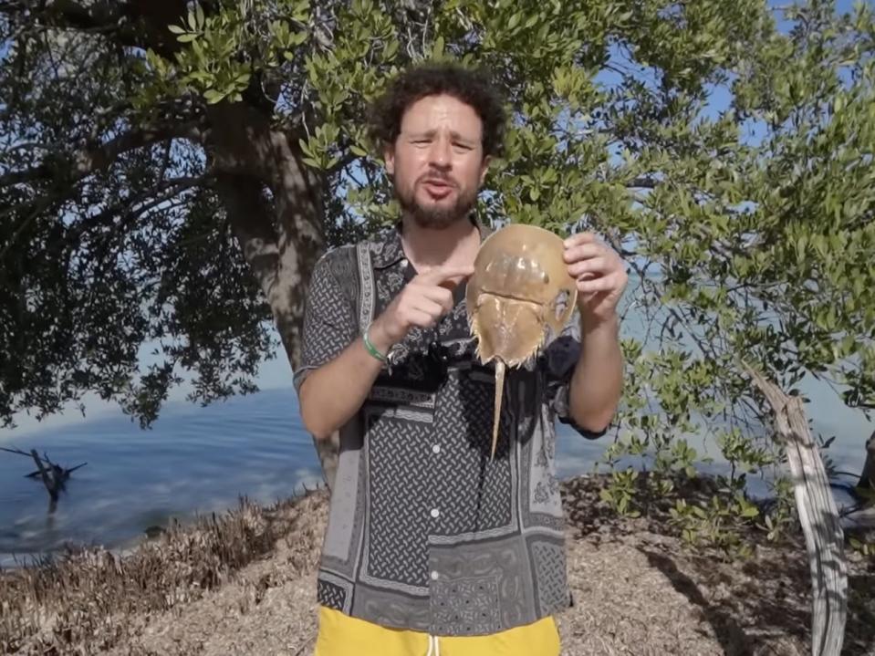 Screenshot from one of Luisito's videos, where he's standing outside holding a shelled animal with a stinger.