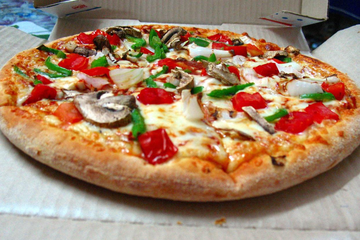 Closeup of Domino's medium pizza with pepperoni, tomatoes, mushrooms, and green bell peppers in an opened delivery box