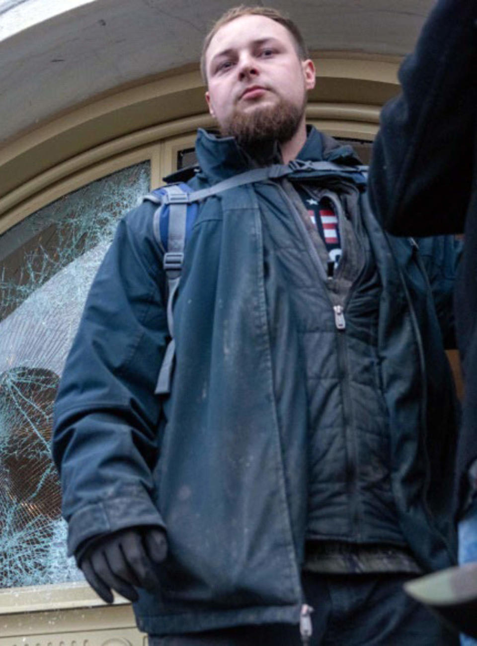 Joshua Lee Atwood stands in front of a broken window at the Capitol. (U.S. District Court for the District of Columbia)