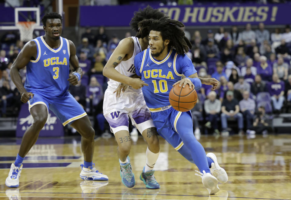 UCLA guard Tyger Campbell drives around Washington guard Koren Johnson with UCLA's Adem Bona (3) behind during the first half of an NCAA college basketball game, Sunday, Jan. 1, 2023, in Seattle. (AP Photo/John Froschauer)