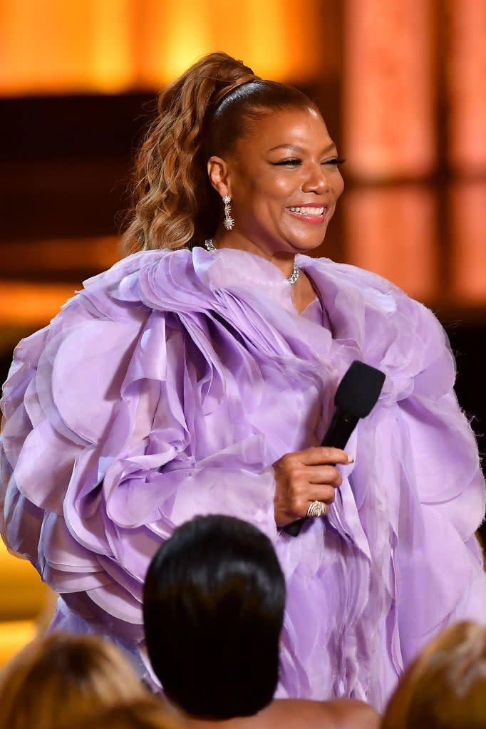 Queen Latifah in a voluminous ruffled gown speaking into a microphone onstage