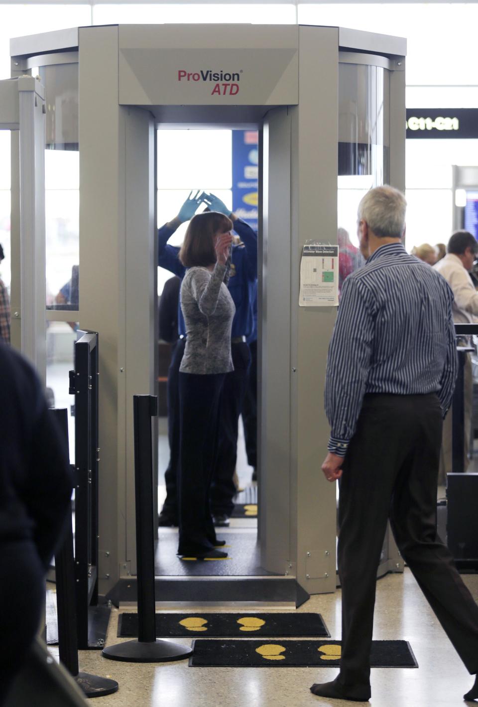 In this Wednesday, Oct. 24, 2012 photo, passengers are scanned at a Terminal C security checkpoint at Logan Airport in Boston using a millimeter wave body scanner, which produces a cartoon-like outline rather than naked images of passengers produced by a similar machine using X-rays. The Transportation Security Administration is deploying more of the millimeter wave machines at seven major U.S. airports where the agency is removing all of the full-body X-ray scanners that have been criticized by privacy advocates. (AP Photo/Charles Krupa)