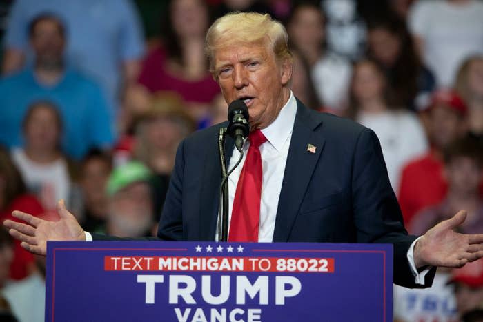 Donald Trump speaks at a rally in Michigan, standing behind a podium that reads "Text Michigan to 88022 Trump Vance."