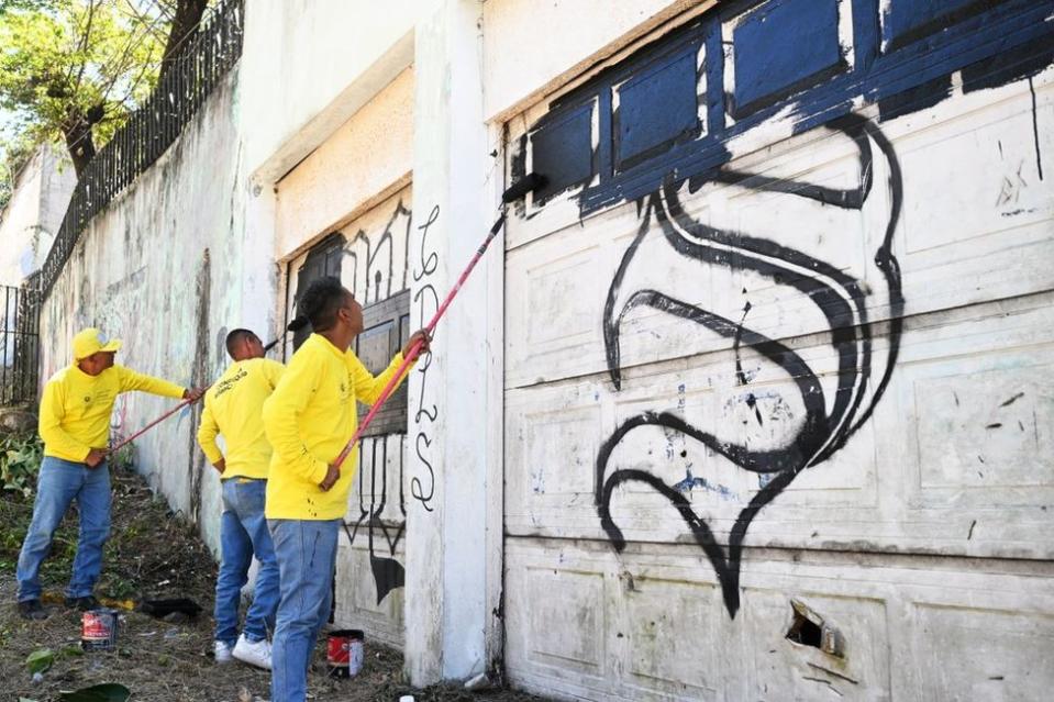 Reclusos del penal La Esperanza, escoltados por guardias, borran un grafiti vinculado a la pandilla Mara Salvatrucha durante un operativo que busca recuperar barrios controlados por pandillas en San Martín, El Salvador el 22 de marzo de 2023. - Hace un año, una ola de Los homicidios en El Salvador llevaron al presidente Nayib Bukeke a iniciar una 