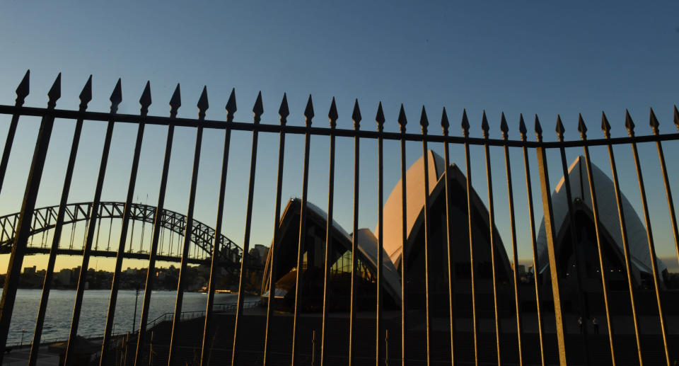 The Sydney Harbour Bridge and the Sydney Opera House is seen behind a high fence at sunset in Sydney. Source: AAP