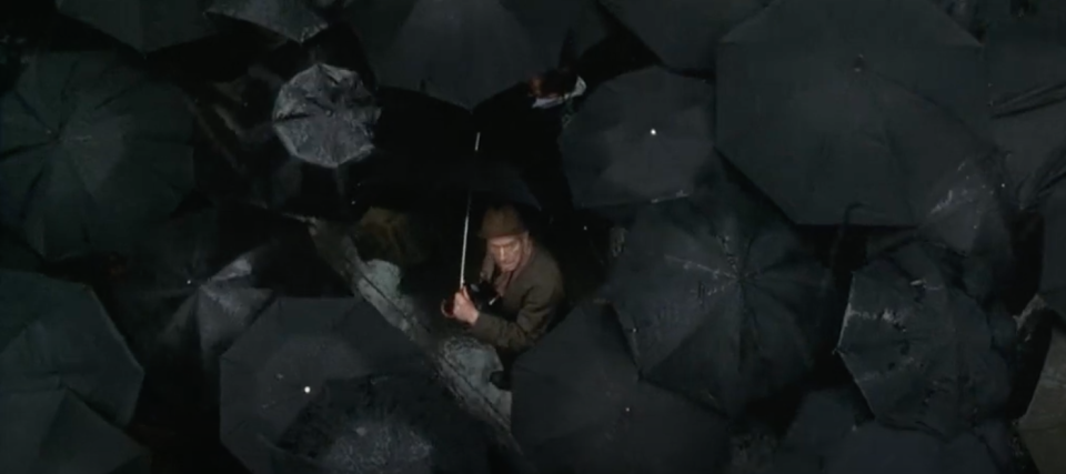 A man in a sea of black umbrellas looking up