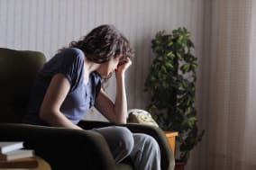 Depressed young woman sitting in chair at home