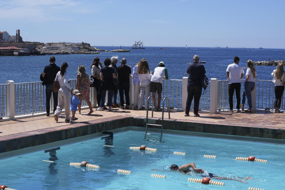 Un grupo de personas frente a una piscina olímpica aguarda el arribo del Belem, el velero con la llama de los Juegos Olímpicos de París, al puerto de Marsella, el miércoles 8 de mayo de 2024. (AP Foto/Laurent Cipriani)