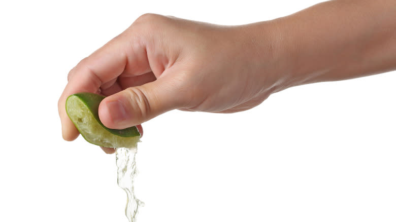 Hand squeezing lime on white background 