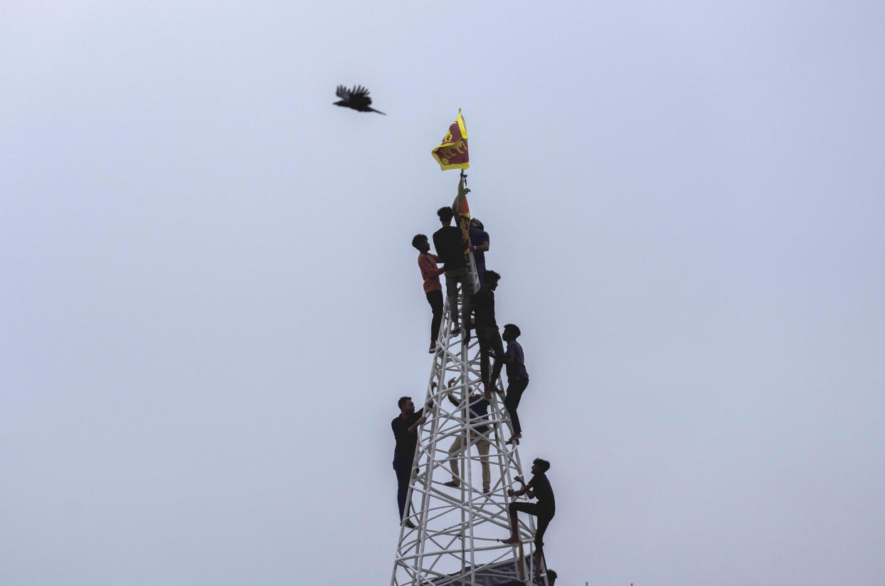 Sri Lankans climb atop a makeshift scaffolding to hoist the national flag near the site of a nationwide protest in Colombo, Sri Lanka, Monday, July 11, 2022. Sri Lanka is in a political vacuum for a second day Monday with opposition leaders yet to agree on who should replace its roundly rejected leaders, whose residences are occupied by protesters, angry over the country's economic woes. (AP Photo/Rafiq Maqbool)