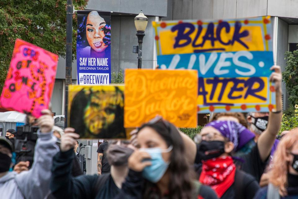 Protesters hold signs as they regroup at Jefferson Square Park following marches as a Breonna Taylor sign looks down upon them Wednesday. Sept. 23, 2020